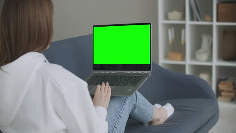 Woman-at-Home-Sitting-on-a-Couch-Works-on-a-Laptop-Computer-with-Green-Mock-up-Screen.-Coronavirus-Covid-19-quarantine-remote-education-or-working-concept.-Girl-Using-Computer-Browsing-through